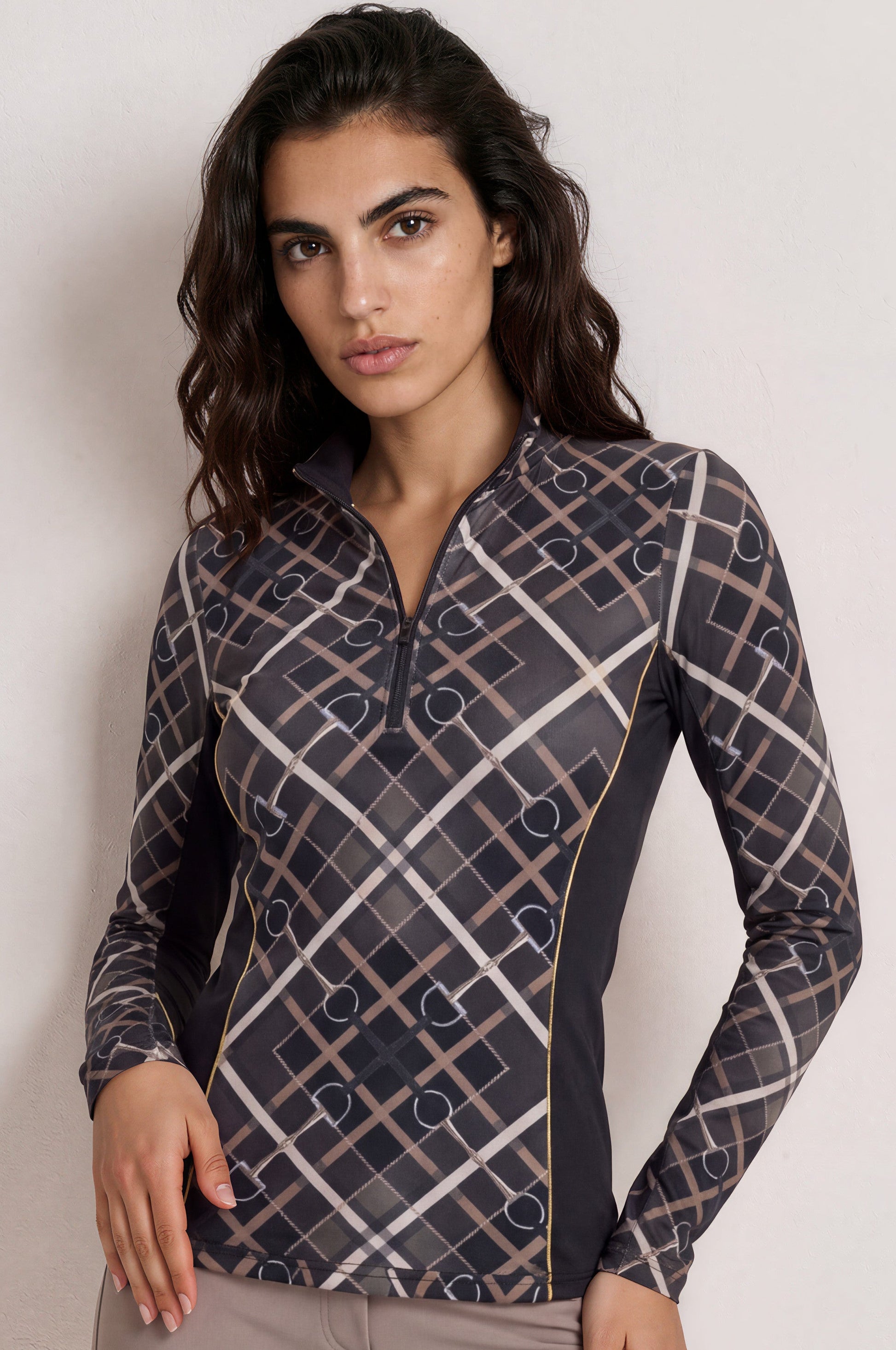 A woman modeling a long-sleeve athletic quarter-zip top with a geometric grid pattern in dark gray, beige, and black, paired with taupe leggings, against a plain light gray studio background.
