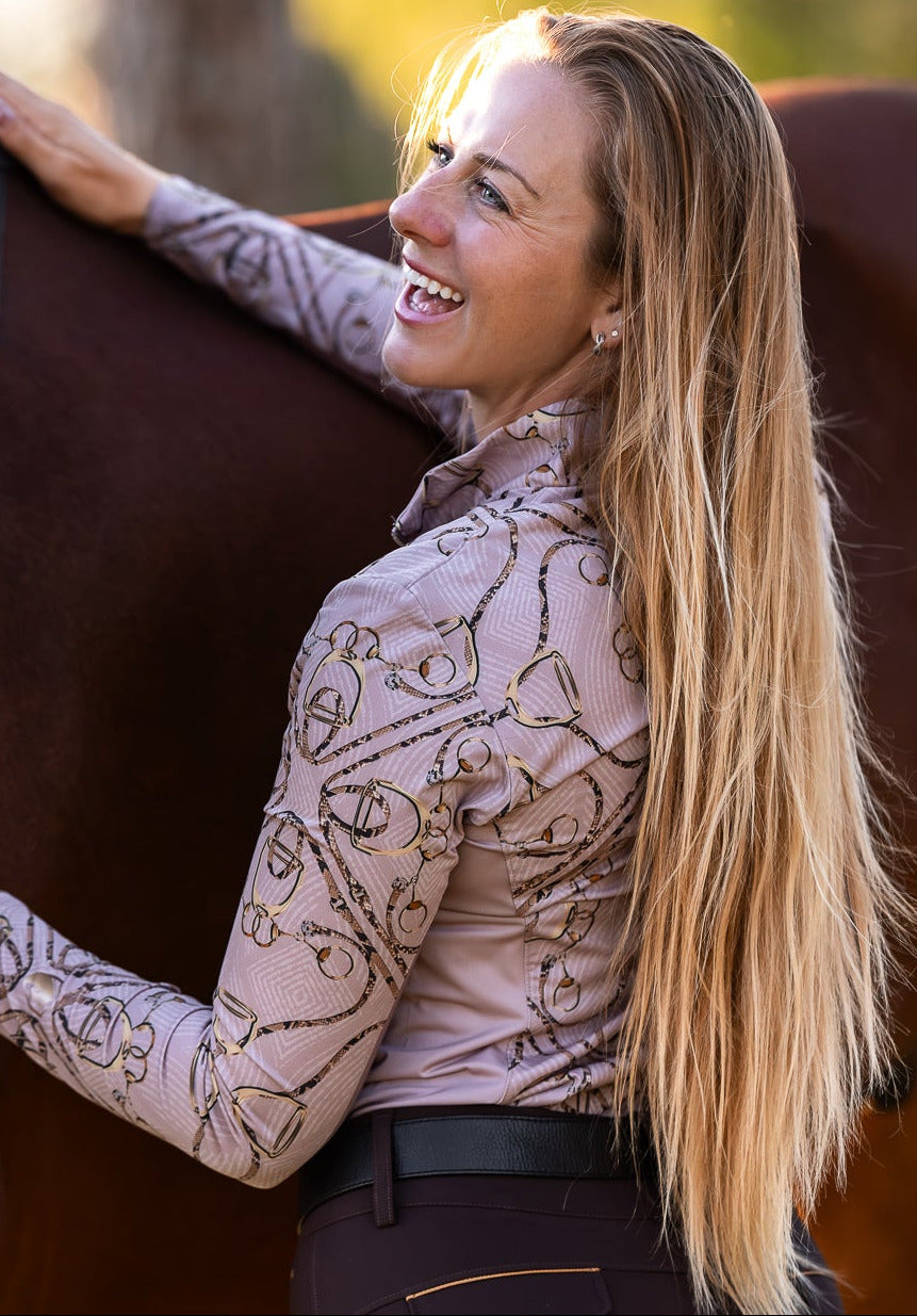 Woman hugging a horse with a pale pink shirt with stirrups and bits on it.