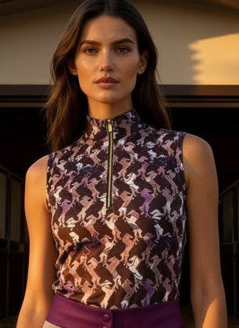 Woman in equestrian attire standing in front of a stable with palm trees.