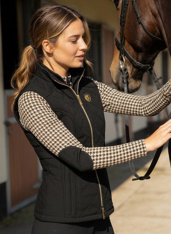 Woman in equestrian attire petting a horse in an outdoor stable setting