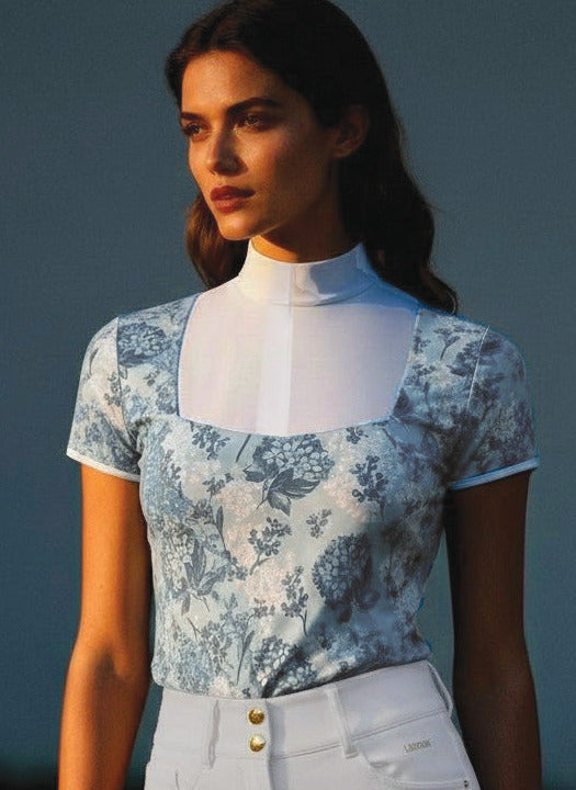 Woman wearing a floral top and white pants standing outdoors with a blurred background
