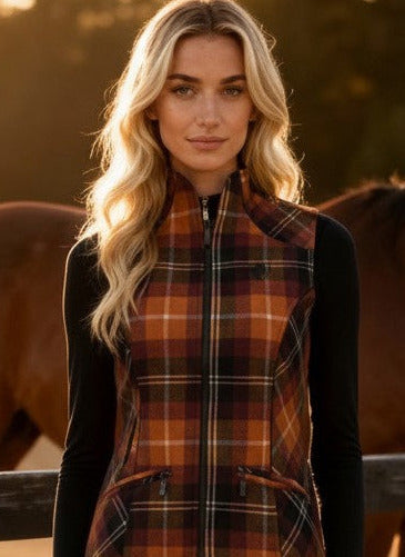 Woman wearing a plaid vest and light pants standing in front of a horse in a paddock.