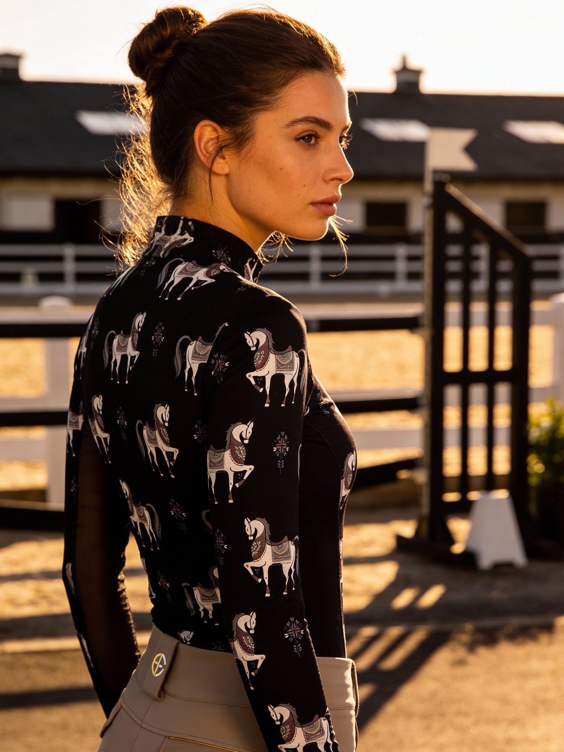 Woman in equestrian attire standing in an outdoor setting with a building in the background