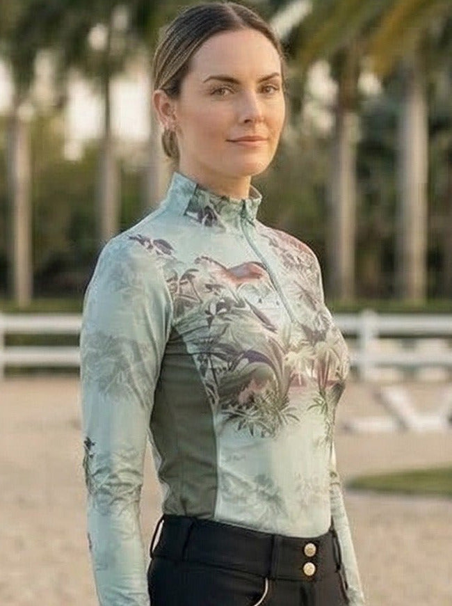 Person in equestrian attire standing in an outdoor arena with palm trees in the background