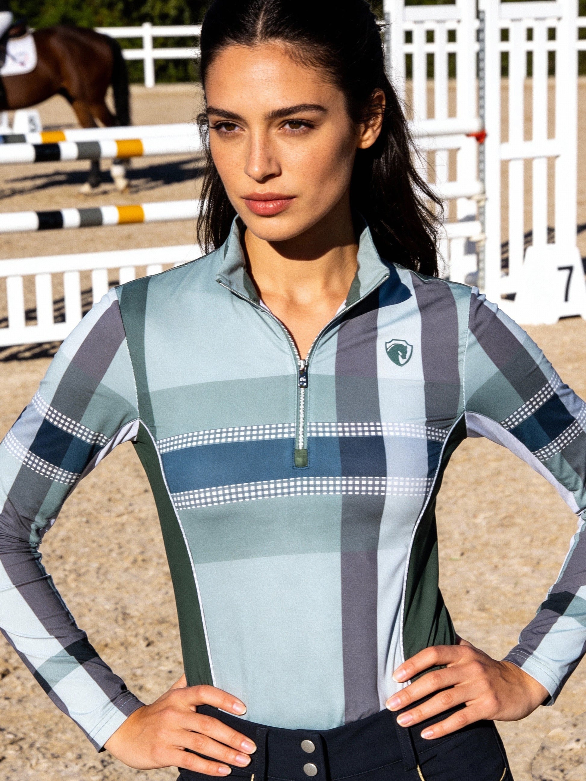 Woman in equestrian attire standing in an outdoor equestrian arena.