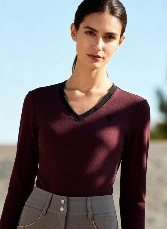 Woman wearing a maroon long-sleeve top and gray riding pants outdoors.