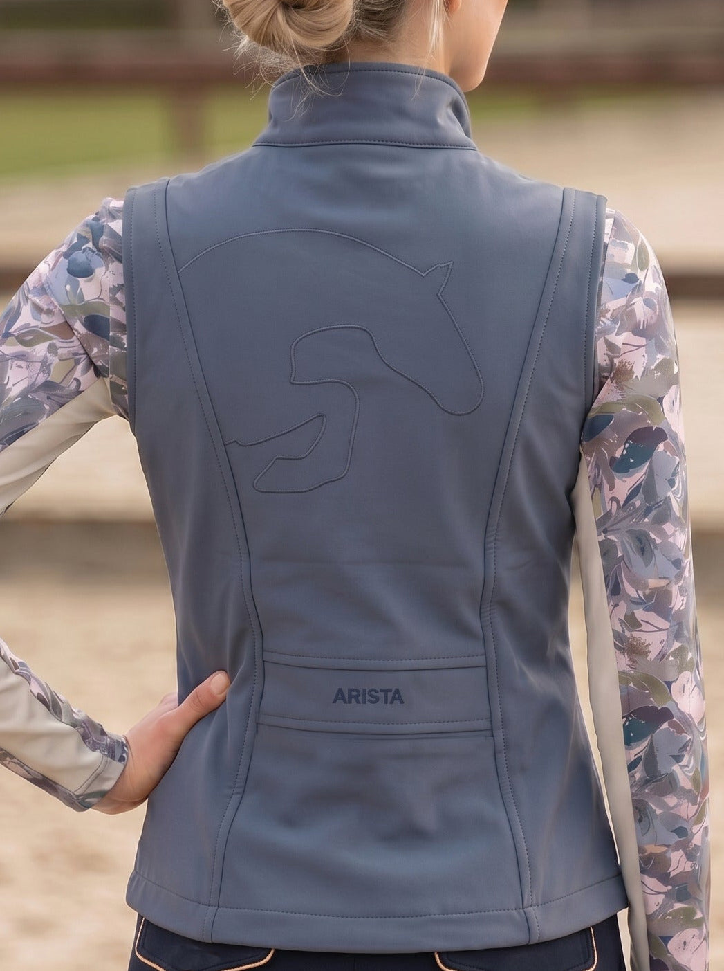 Person wearing a blue equestrian vest with floral sleeves in an outdoor setting.