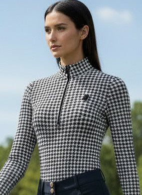 Woman in checkered shirt and dark pants walking on grass with trees in the background