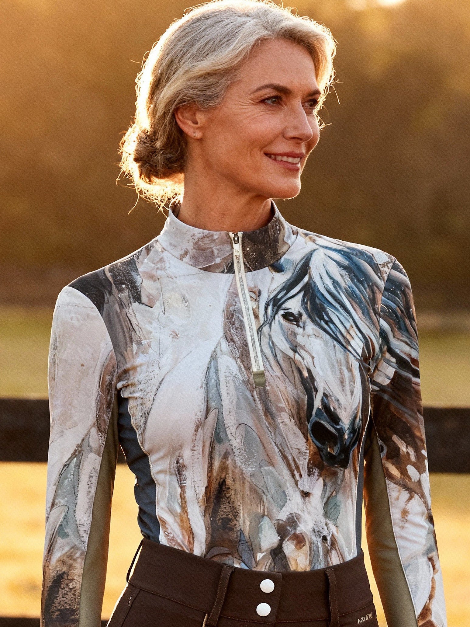 Woman in equestrian attire standing in a field with a horse in the background