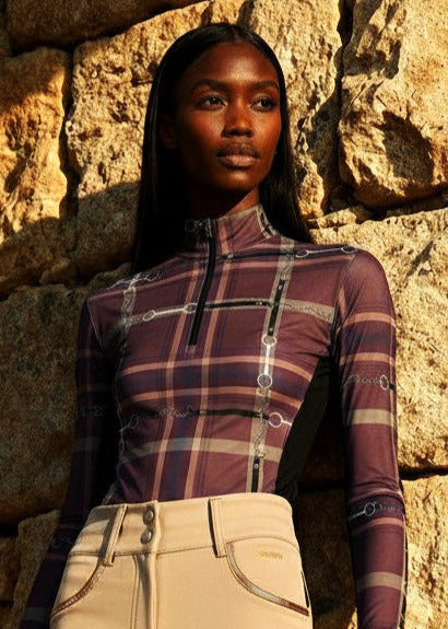 Person wearing a plaid top and beige pants against a stone wall.