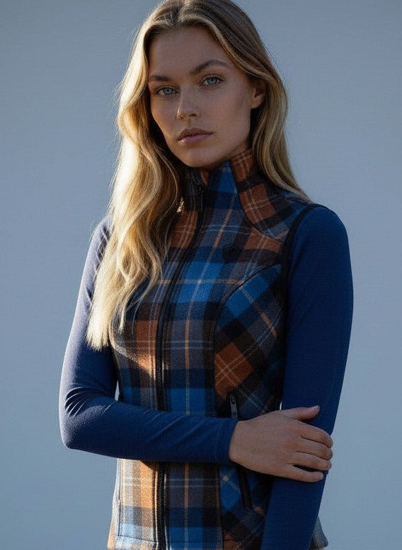 Woman wearing a blue long-sleeve top and plaid vest against a plain background