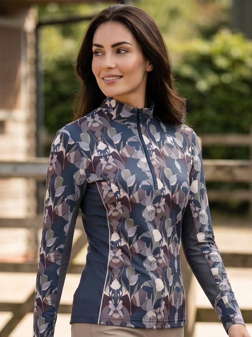 Woman in equestrian attire walking in an outdoor setting with a stable in the background