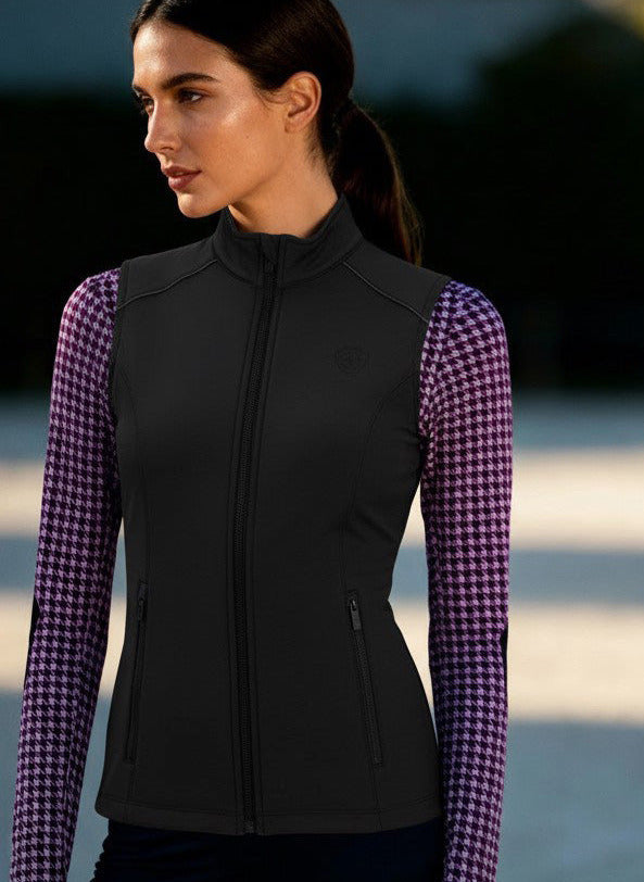 Woman wearing a black vest over a purple checkered shirt with a blurred outdoor background