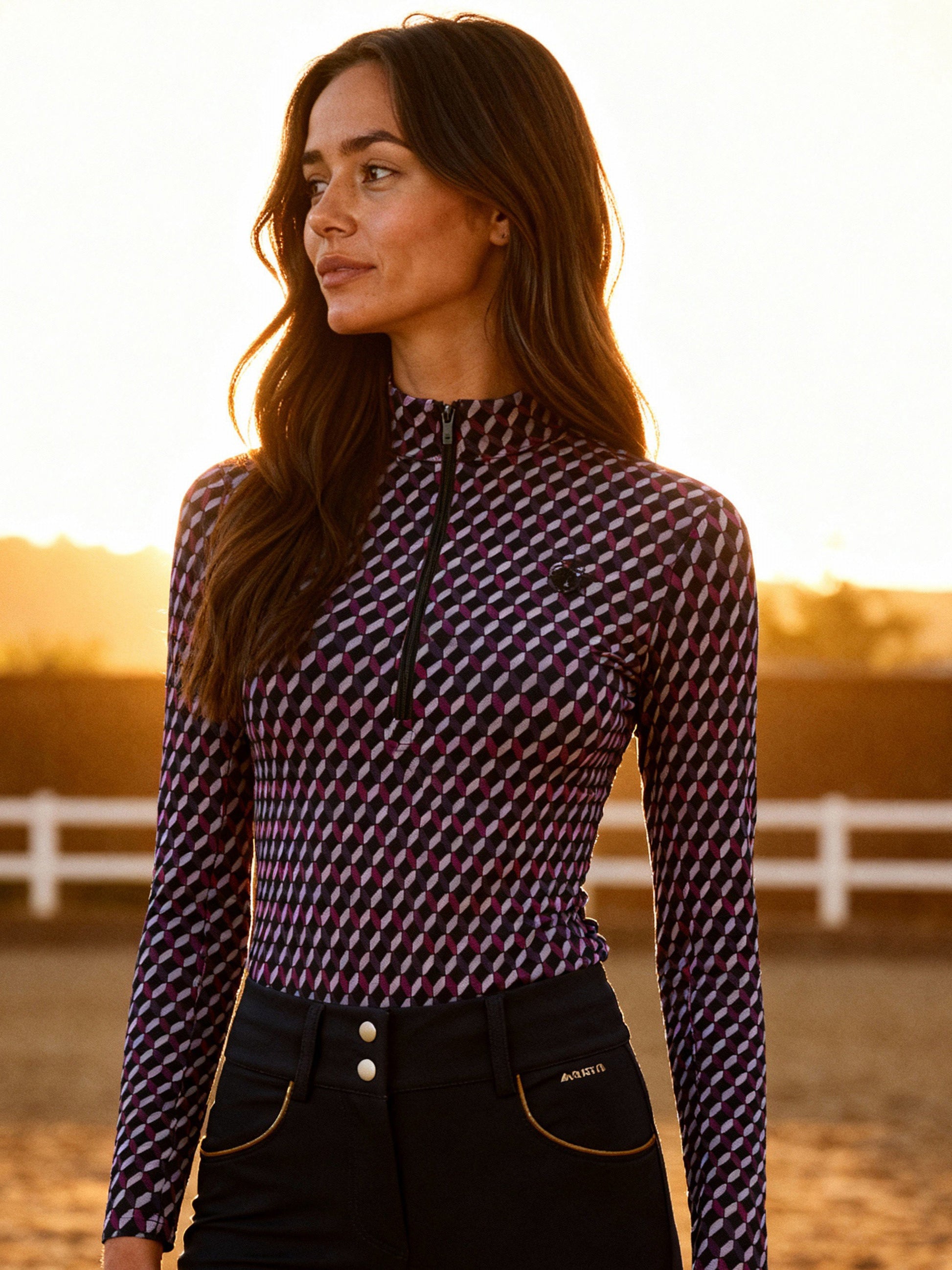 Woman wearing a checkered long-sleeve top and dark pants in an outdoor setting with a sunset.