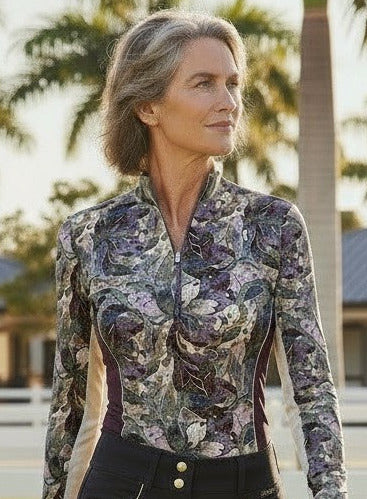 Woman in equestrian attire walking on grass with stables in the background