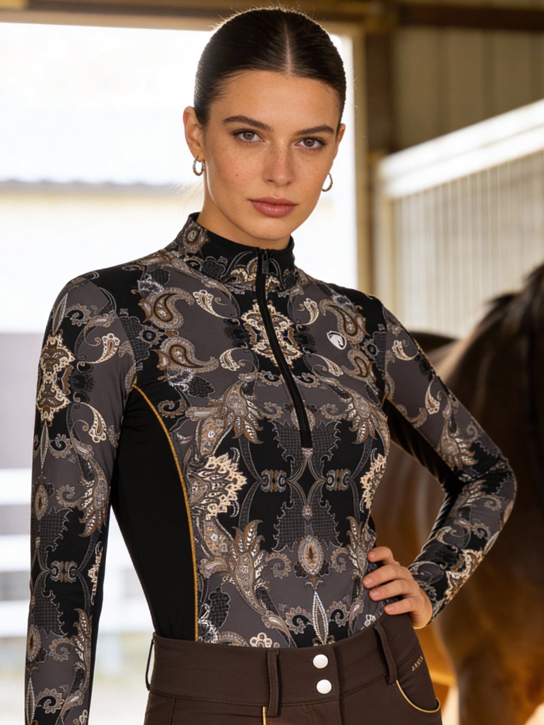Woman in equestrian attire standing next to a horse in a stable.