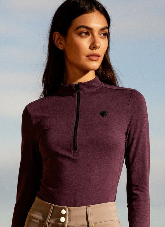 Woman wearing a purple long-sleeve top and beige riding pants outdoors.