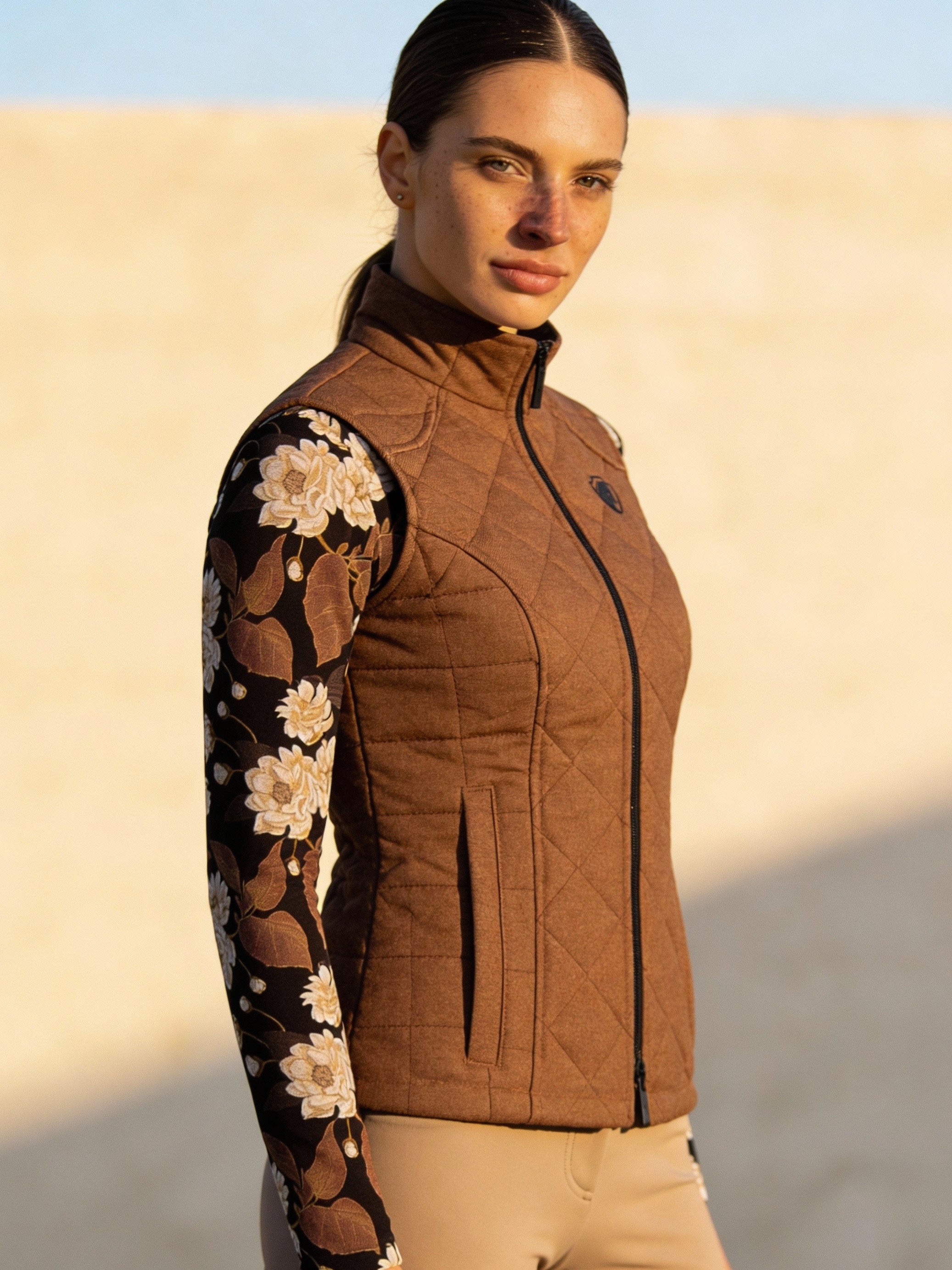 Woman wearing a brown quilted jacket with floral sleeves against a beige wall.